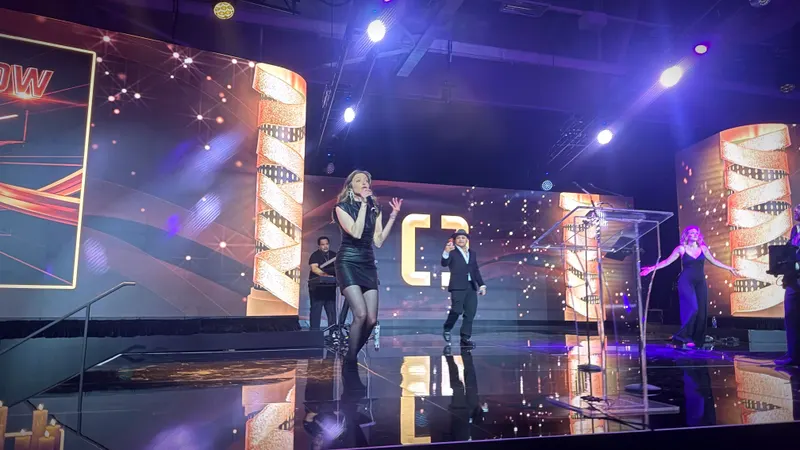 Female vocalist centre stage between illuminated gold columns at an awards gala