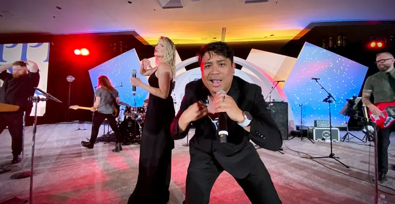 uRequest Live vocalist lunging toward the camera with the band playing behind