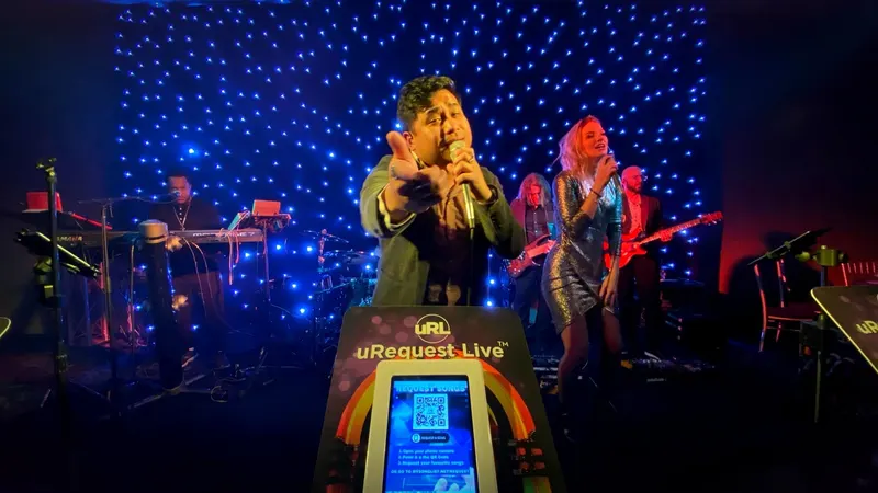 Vocalist pointing at the camera beside a request kiosk showing its QR code
