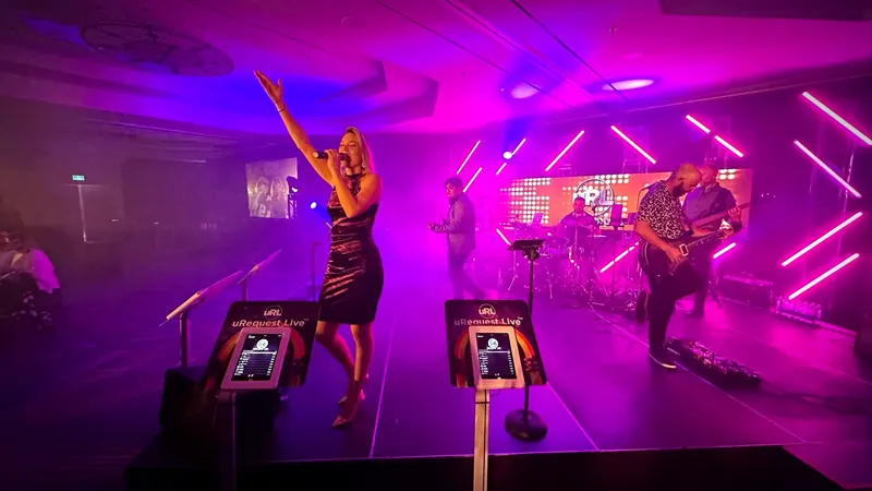 Female vocalist with her arm raised on a magenta-lit ballroom stage with two request kiosks