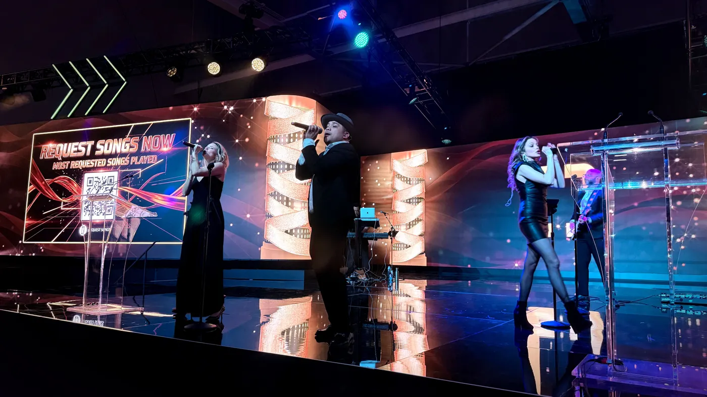 uRequest Live vocalists performing at a corporate event beside a Request Songs Now QR screen